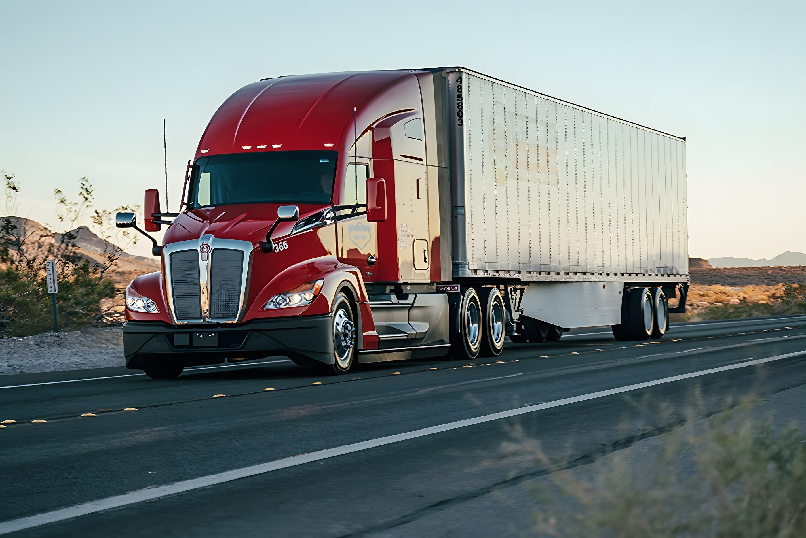 A red highway tractor pulling a 53-foot dry van down a two-lane highway at sunset